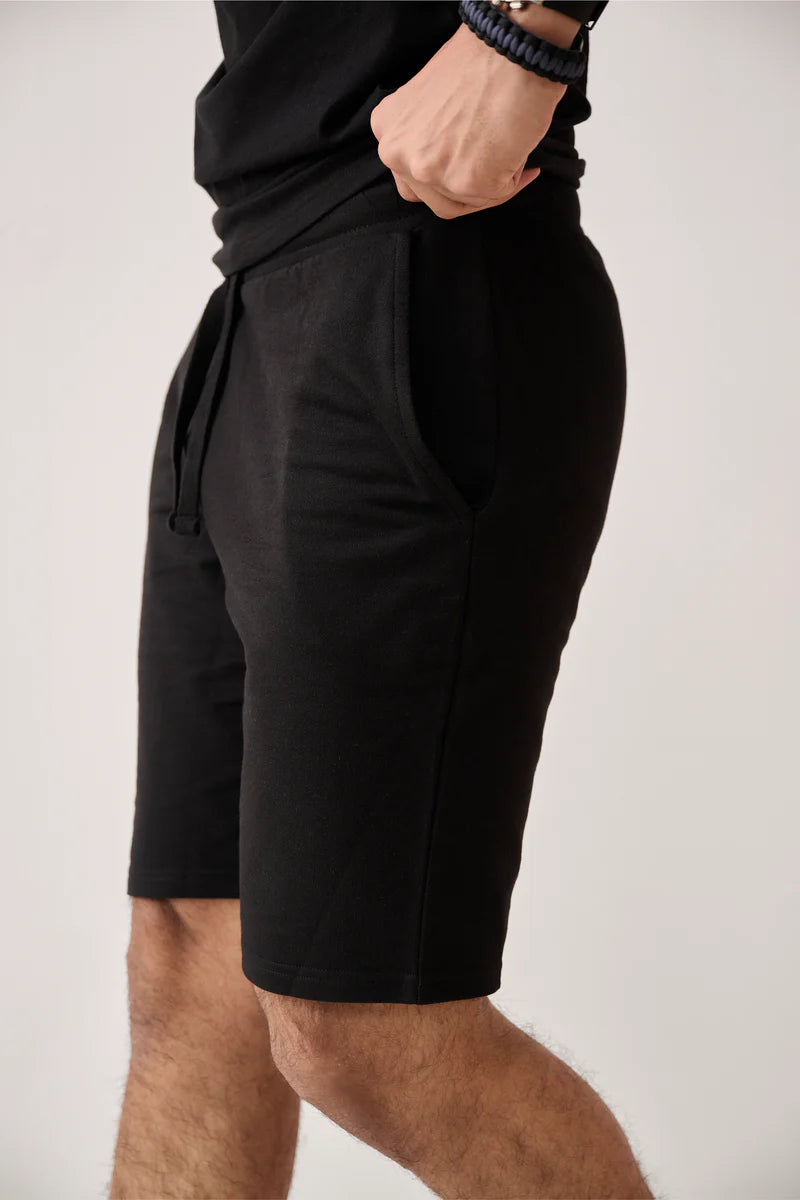 A man wearing Terry Shorts Black with his right hand in the pocket, showing a close-up of the shorts' side profile and his wrist.